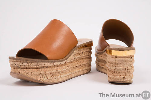 Pair of orange slide platform sandals with cork platform and gold band trim at heel