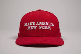 Red baseball cap with white embroidered text “Make America” and white dimensional embroidered “…