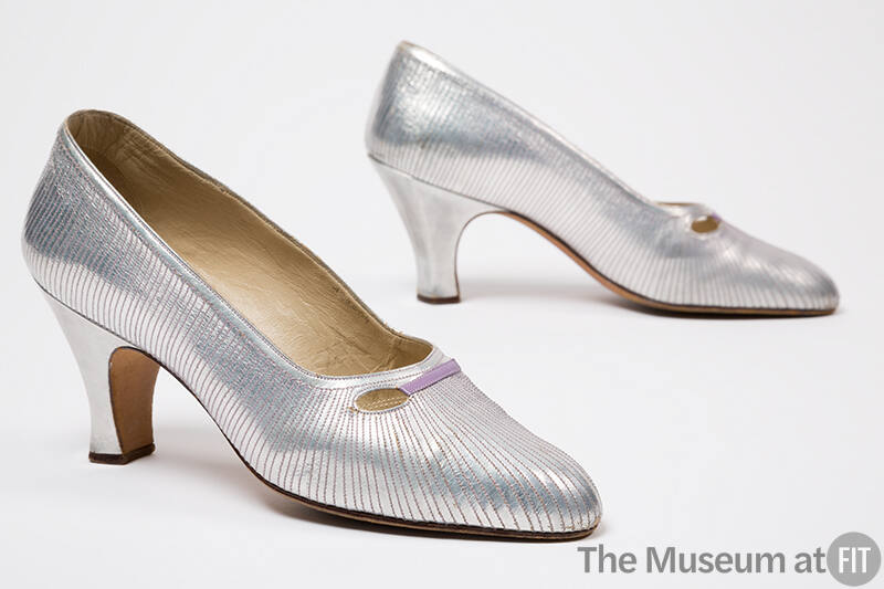 Pair of silver evening pumps with allover contrasting linear topstitching and eyelet cutouts at…