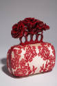 Off-white hand bag with red lace overaly, red metal knuckle handle with red roses