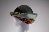 Back view of black straw hat showing light blue lined brim turned up with pink rosebuds and gre…