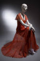 Seated view of orange evening dress showing pieced openwork overdress and orange camisole style…