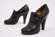 Pair of black high heel shoes with high vamp and attached winding faux strap with buckle at ank…