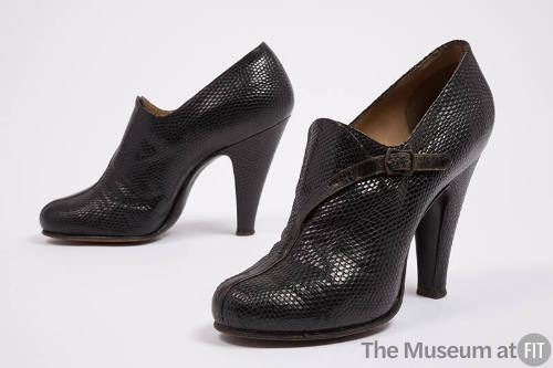 Pair of black high heel shoes with high vamp and attached winding faux strap with buckle at ank…