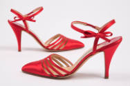 Side views of pair of red pointy toe high heel sandals with ankle straps with tiny bow detail 