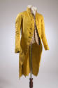 Man’s yellow/green cutaway jacket with stand collar and large self-covered buttons dressed with…