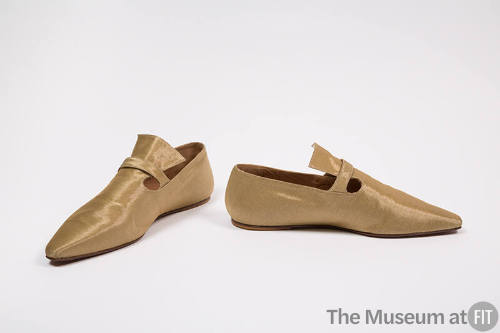 Pair of gold metallic flat shoes with pointed toe and strap over high, flared vamp tab