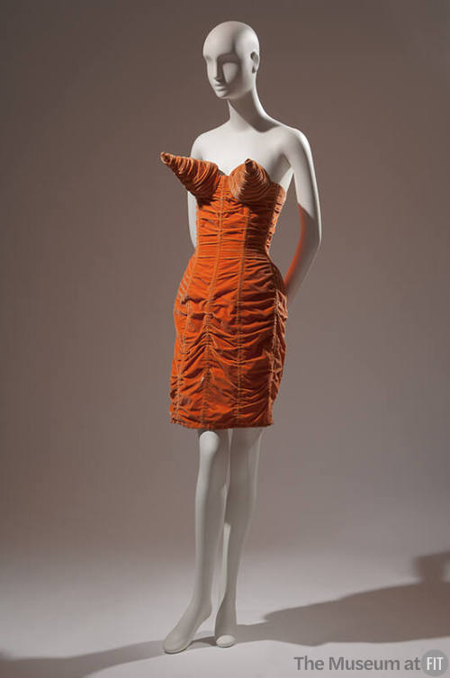Ruched orange velvet strapless dress with large cones at bust, above-the-knee length 