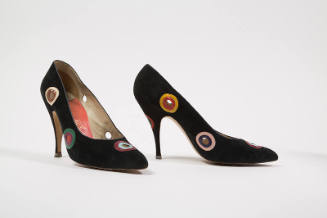 Pair of black high heel pumps with circular cut-outs throughout surrounded by concentric circle…