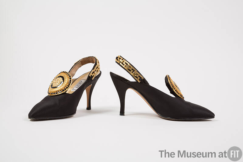Pair of black slingback pumps with large black and gold Medusa head ornament on vamp, gold meta…