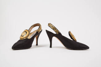 Pair of black slingback pumps with large black and gold Medusa head ornament on vamp, gold meta…