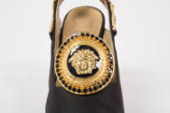 Detail view of black slingback pump showing black and gold ornament on vamp of Medusa head outl…