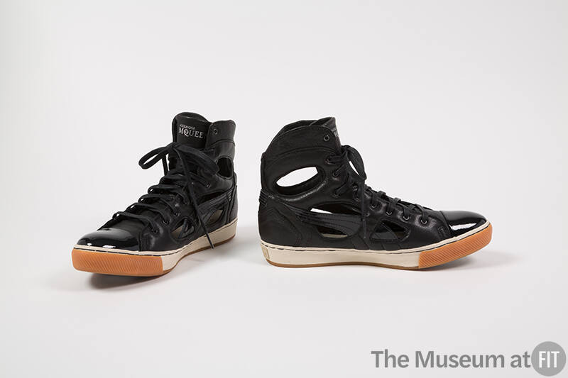 Pair of black high top sneakers with patent leather toe cap and cut outs along shank and ankle …