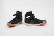 Pair of black high top sneakers with patent leather toe cap and cut outs along shank and ankle …