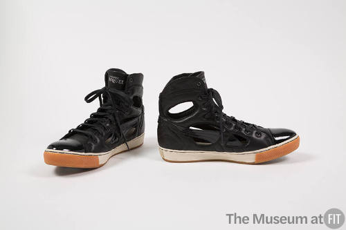 Pair of black high top sneakers with patent leather toe cap and cut outs along shank and ankle …
