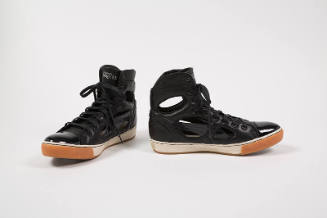 Pair of black high top sneakers with patent leather toe cap and cut outs along shank and ankle …
