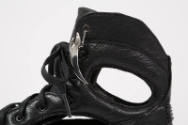 Detail view of black high top sneaker showing cut out at ankle and metal charm attached to top …