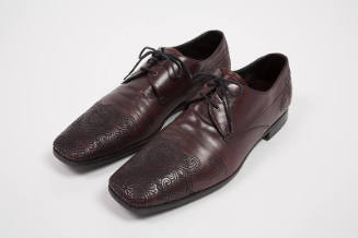 Man's dark red/brown lace up shoes with topstitched design of scrolling lines, swriling clouds,…