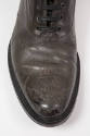 Detail view of man’s dark grey/brown ankle boot showing tooled design of a historical sailing s…