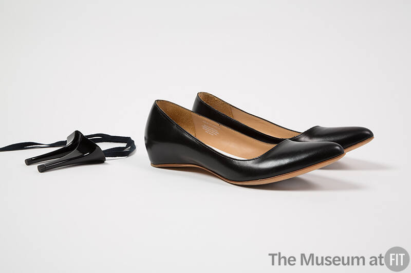 Pair of black flat shoes pictured with necklace made of shoe lace and two black high heels