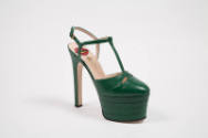 Green high heel platform t-strap shoe with Gucci logo, yellow star and red mouth visible on bei…