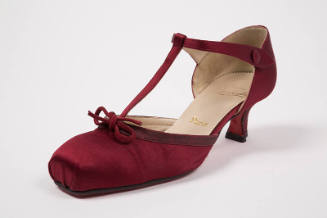 Dark red T-strap shoe with square toe box, small bow at vamp, low heel and gold “Paris” visible…