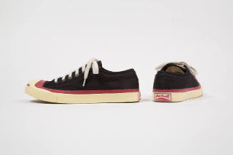 Pair of black sneakers with red trim around white sole and toe cap and red “Jack Purcell” writi…