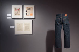 Denim: Fashion’s Frontier exhibition installation view of a pair of jeans and art on the wall
