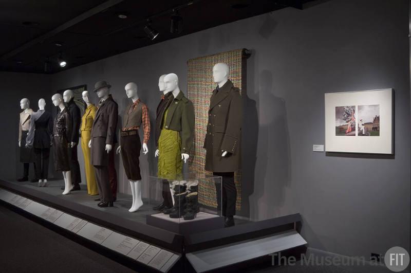 His and Hers_38 2010.82.1 (man's skirt ensemble), 2010.88.1 (ensemble), 2001.80.2 (textile wall), 2010.93.1 (suit), 2010.90.1 (jumpsuit), 2010.79.1 (pantsuit), 2010.91.2 (suit), 2010.91.1 (hat ensemble), 2010.85.1 (ensemble), 2010.85.2 (suit), 2006.11.3 (textile wall), 2010.62.1 (ensemble), 2010.62.2 (coat ensemble) (boots for both in case)