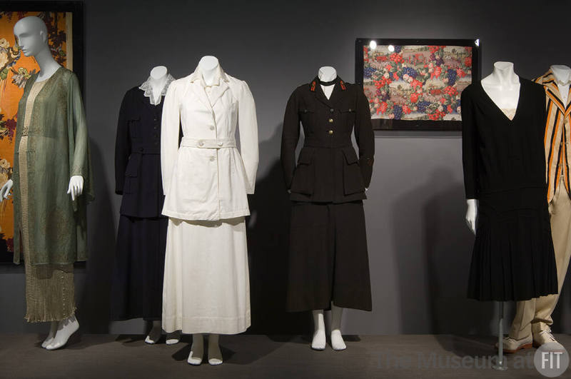 Fashion and Politics_36 Left to right 80.262.1 and 2001.67.2 (dress and coat), P88.74.2 (suit), P87.25.1 (white suit), 84.55.1 (uniform), 81.224.637 (textile wall), 80.13.12 (black dress), P89.40.25 (striped jacket) 