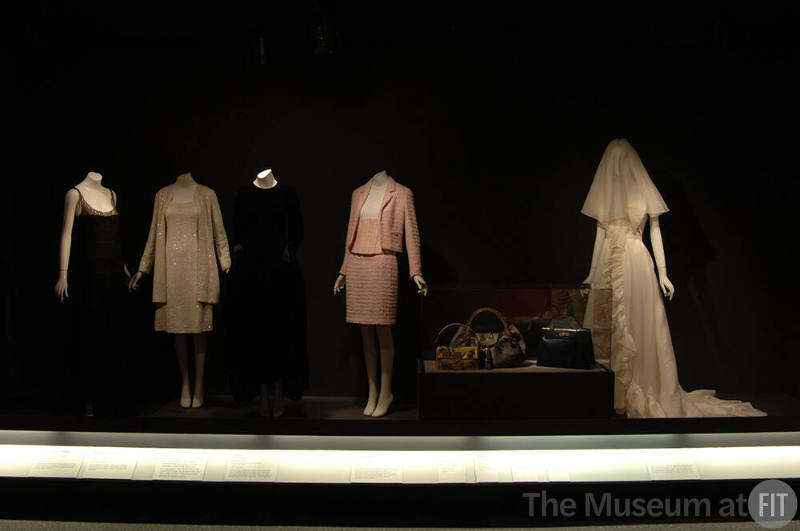 Luxury_05 Left to right 77.89.1 (lace dress), 91.255.7 (sequined ensemble), 91.231.1 (velvet dress), 94.80.1 (suit), 2007.25.1 (bag case), 2007.25.2 (bag case), 2002.96.18 (bag case), 2007.17.1 (wedding dress)