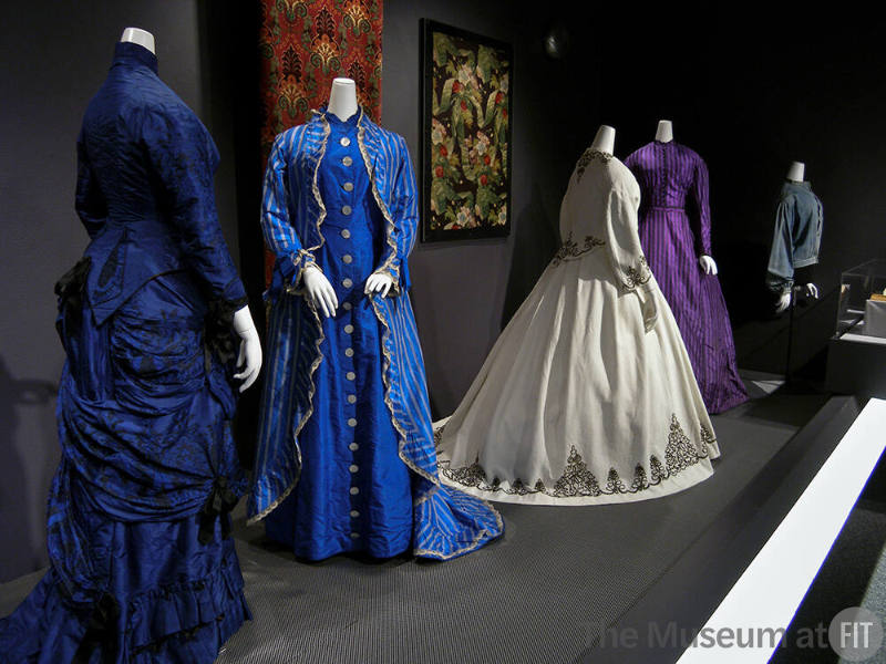 Rainbow_24 Left to right 70.65.6 (blue dress), P94.8.1 (blue striped dress), P90.77.1 (textile wall), P90.22.2 (white dress), 84.31.2B (textile wall), 2006.43.1 (purple dress), P87.43.3 (jacket)
