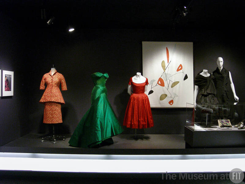 Rainbow_62 Left to right 92.145.1 (suit), 91.241.129 (green gown), 95.65.1 (red dress), P89.49.3 (textile wall), 69.170.5 (hat case), 74.107.243 (pin, earrings case), 79.169.6 (bag and shoes case), 82.208.3 (wrap dress),  71.265.7 (black dress)