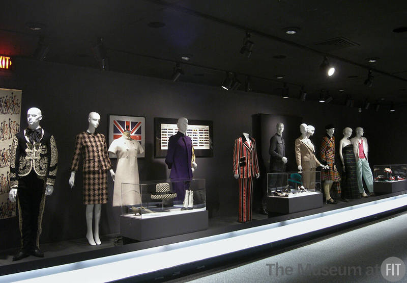 Tailor_7 Left to right 2002.22.1 (textile wall), P88.57.2 (suit), 78.55.23 (plaid suit), 95.57.7 (white dress), 68.143.137 (shoes case), 80.130.31 (hat case), P90.87.9 (boots case), 91.181.13 (flag scarf wall), 81.204.1 (textile wall), 84.79.1 (purple suit), 84.23.1 (suit hidden), 2001.55.1 (striped suit), 91.210.34 (shoes case), 89.54.21 (green hat case), 79.169.8 (shoes case), 76.27.2 (grey pantsuit), 86.101.17 (beige suit), 91.255.4 (tuxedo hidden), P88.45.2 (tartan ensemble), 89.131.1 (tartan dress), 89.89.1 (pastel ensemble), 90.59.4 (shoes case), P87.14.2 (hat case), 87.113.1 (bag case), 84.190.1 (shoes case)