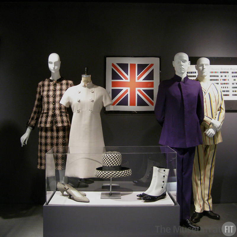 Tailor_11 Left to rght 78.55.23 (plaid suit), 95.57.7 (white dress), 68.143.137 (shoes case), 80.130.31 (hat case), P90.87.9 (boots case), 91.181.13 (flag scarf wall), 84.79.1 (purple suit), 84.23.1 (suit), 81.204.1 (textile wall)