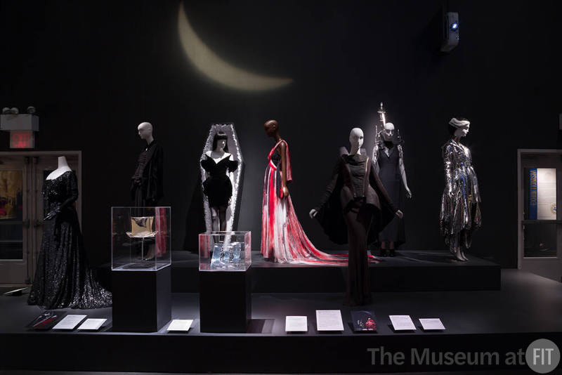 Exhibitionism_23 Left to right 2007.23.2 (beaded dress), 2007.2.1 (black ensemble), 2008.5.1 (hat case), 99.80.1 (velvet dress), 2018.3.2 (earrings case), 2008.55.1 (gown with red),  2010.94.1 (cape skirt ensemble), 2009.10.1 (ensemble with medical parts),  2011.58.1 (silver ensemble)