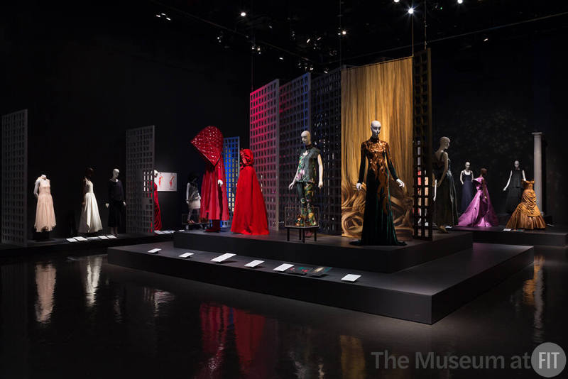 Exhibitionism_25 Left to right  P83.39.7 (dress), 72.61.91 (white dress), 88.157.3 (top and skirt), 2015.8.1 (red ensemble), 2002.36.1 (red cape), 2008.45.1 (pants ensemble and shoes case), 2005.24.1A  (textile hanging), 2013.2.1 (gold and velvet gown), 2010.37.12 (denim dress back), 2005.2.1 (purple gown), 2002.18.1 (black dress), 91.241.128 (gold gown)