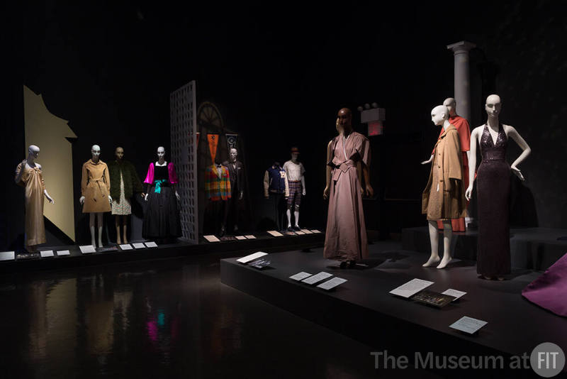 Exhibitionism_42 Left to right 82.3.9 (dress), 82.193.4 (tan dress), 2010.86.30 and 2014.36.1 (dress and coat), 84.145.1 (gown), 87.111.4 (plaid jacket), 2006.16.1 (grey suit),  89.90.1 (baseball jacket), 75.85.20 (hat), P89.8.4 (shirt), 82.124.3 (shorts), 2010.1.48 (wrap dress and belt), 68.143.6 (coat and dress), 88.88.1 (orange ensemble), 68.143.68 (grey halter dress)