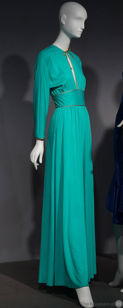 Green long sleeve jumpsuit with gold trimmed key hole neck and gold tie extending to wide waist…