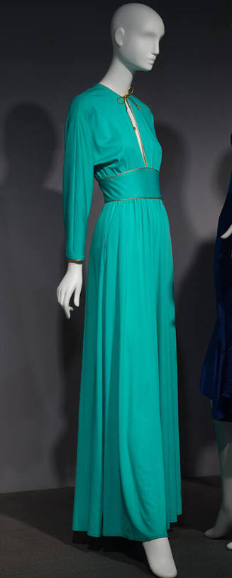 Green long sleeve jumpsuit with gold trimmed key hole neck and gold tie extending to wide waist…