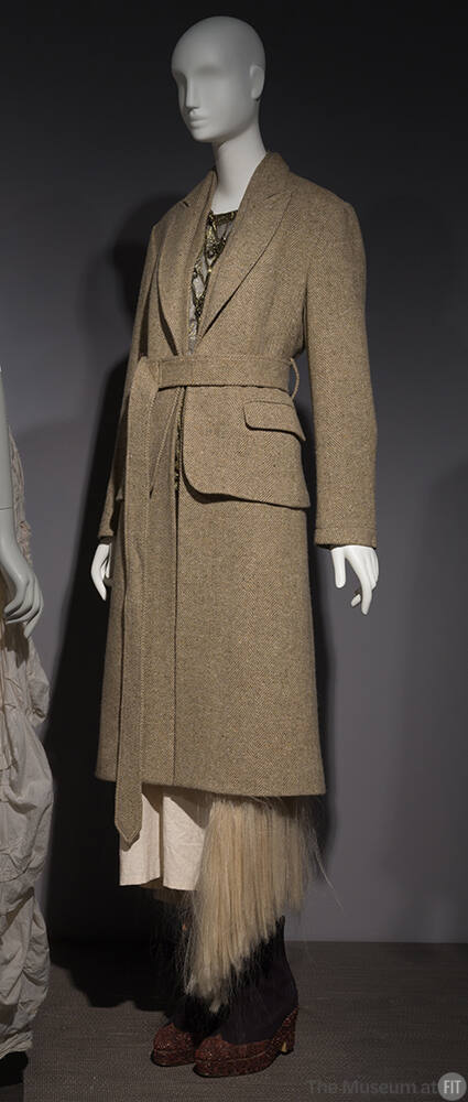 Green tweed belted coat over gold lame blouse and calf length muslin skirt with beige hair frin…