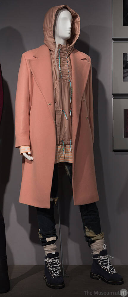 Man’s beige notch collar coat, tan jacket with hood, blue distressed denim jeans and blue hikin…