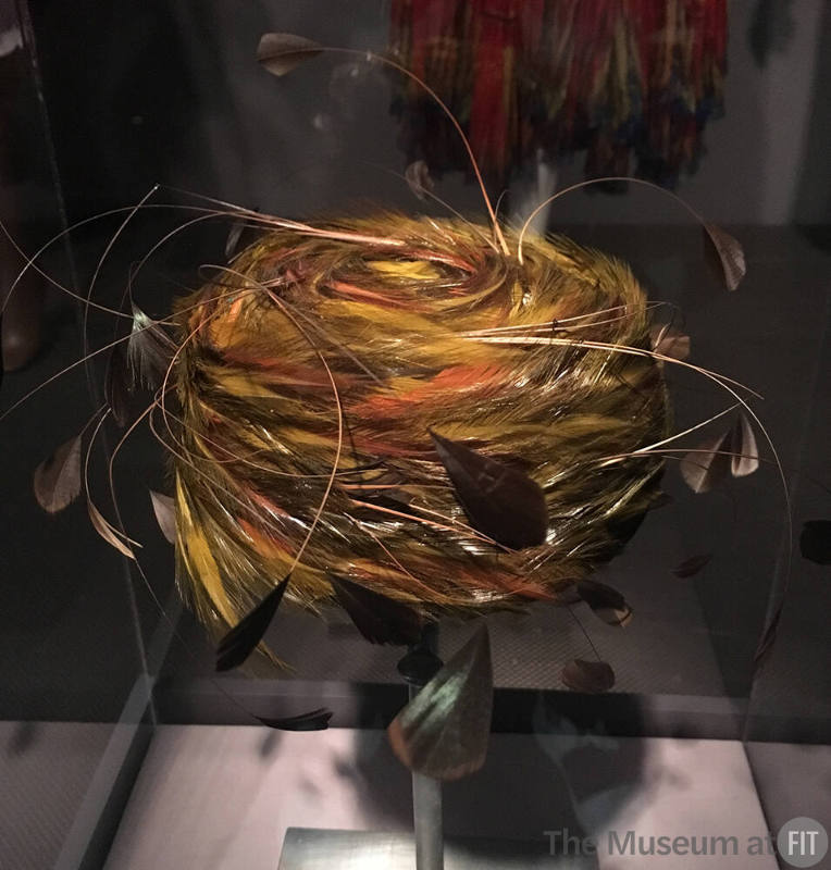 Small pillbox hat of wrapped green, black and brown feathers and projecting stripped quills